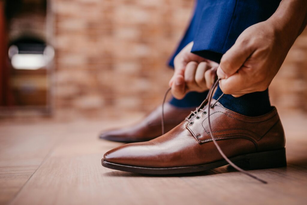 Close-up of a man tying laces on elegant brown leather shoes indoors.