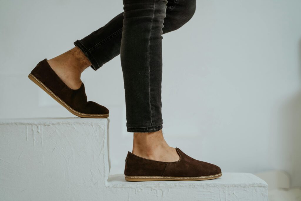 Close-up of brown suede loafers paired with denim jeans stepping down white stairs, showcasing modern style.