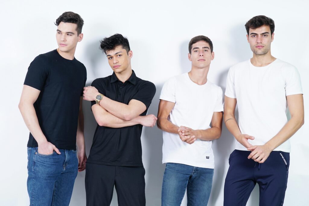 Group of four young men in casual outfits posing in studio with white background.
