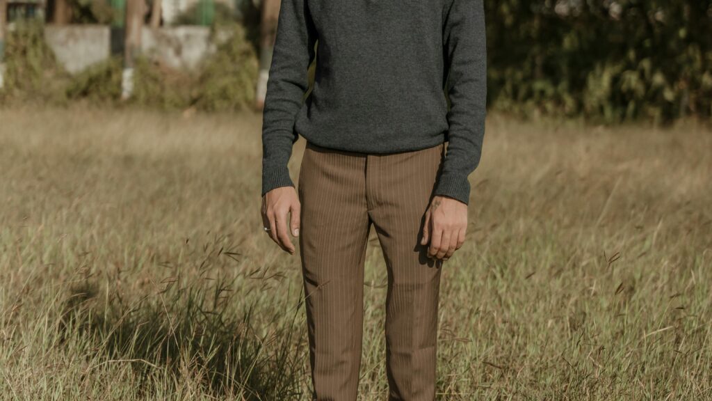 A cropped view of a man standing in a rural grassland wearing a pullover and trousers.