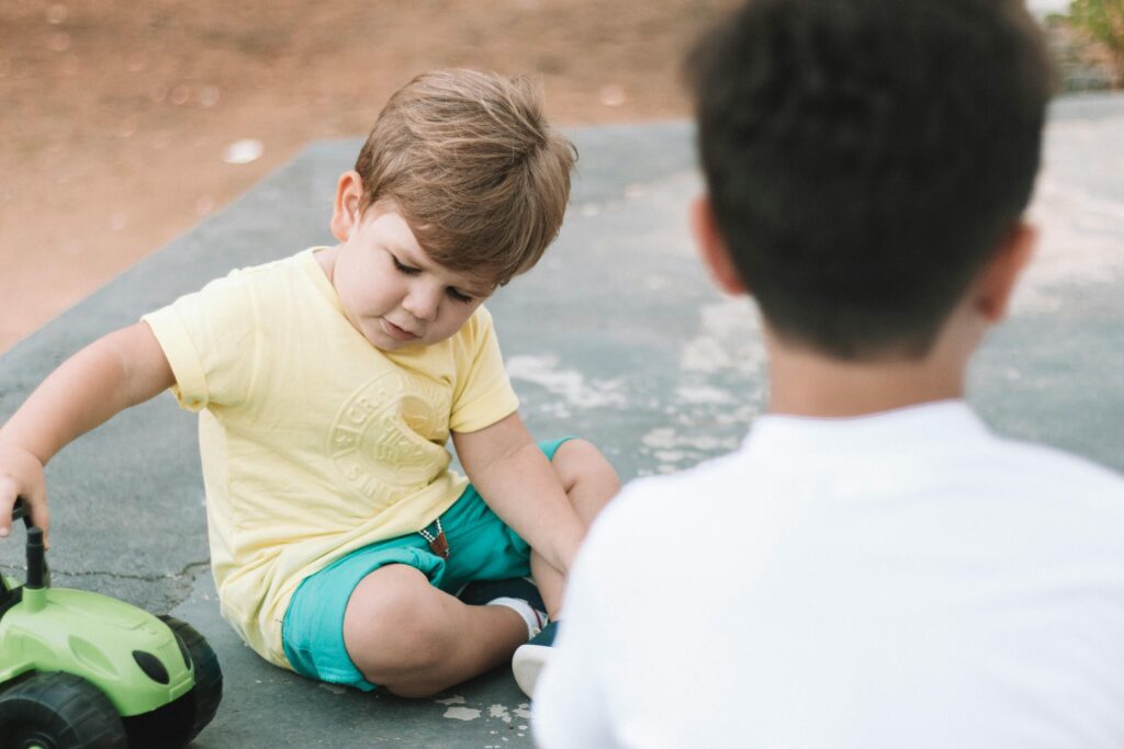 Two young boys playing outdoors with a toy car, enjoying summer fun.