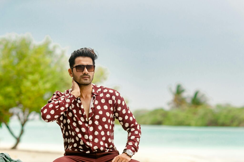 A fashionable man posing on a beach in the Maldives wearing stylish attire.