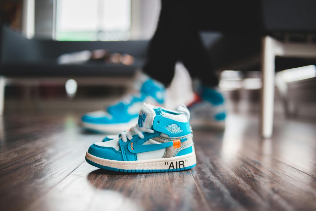 Tiny vibrant sneakers for baby on wooden floor in bright room in daylight on blurred background